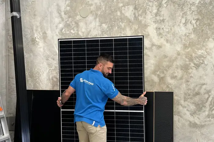 OffXgrid installer carrying a large solar panel across the workshop floor